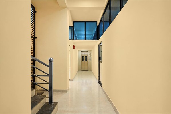 A corridor with a staircase on the left, a fire alarm on the wall, and an elevator on the right. - Townhouse GT Road Dadri (Dadri)