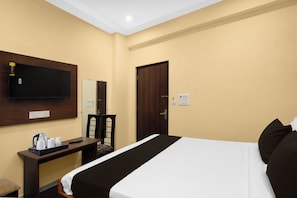 A hotel room with a bed, a desk with a flat-screen TV, a chair, and a wooden door. - Townhouse GT Road Dadri (Dadri)