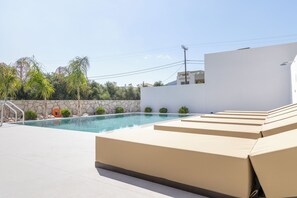 Una piscina con sillas de descanso, un muro de piedra y un cielo despejado.