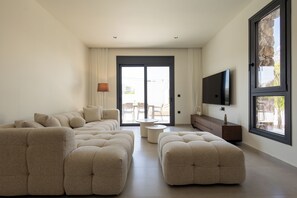 Ein modernes Wohnzimmer mit Ecksofa, Hocker und einem flachbildfernseher an der Wand.