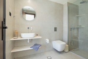 Ein modernes Badezimmer mit einem großen Spiegel, einem weißen Waschbecken, einer Toilette und einer Duschkabine aus Glas.