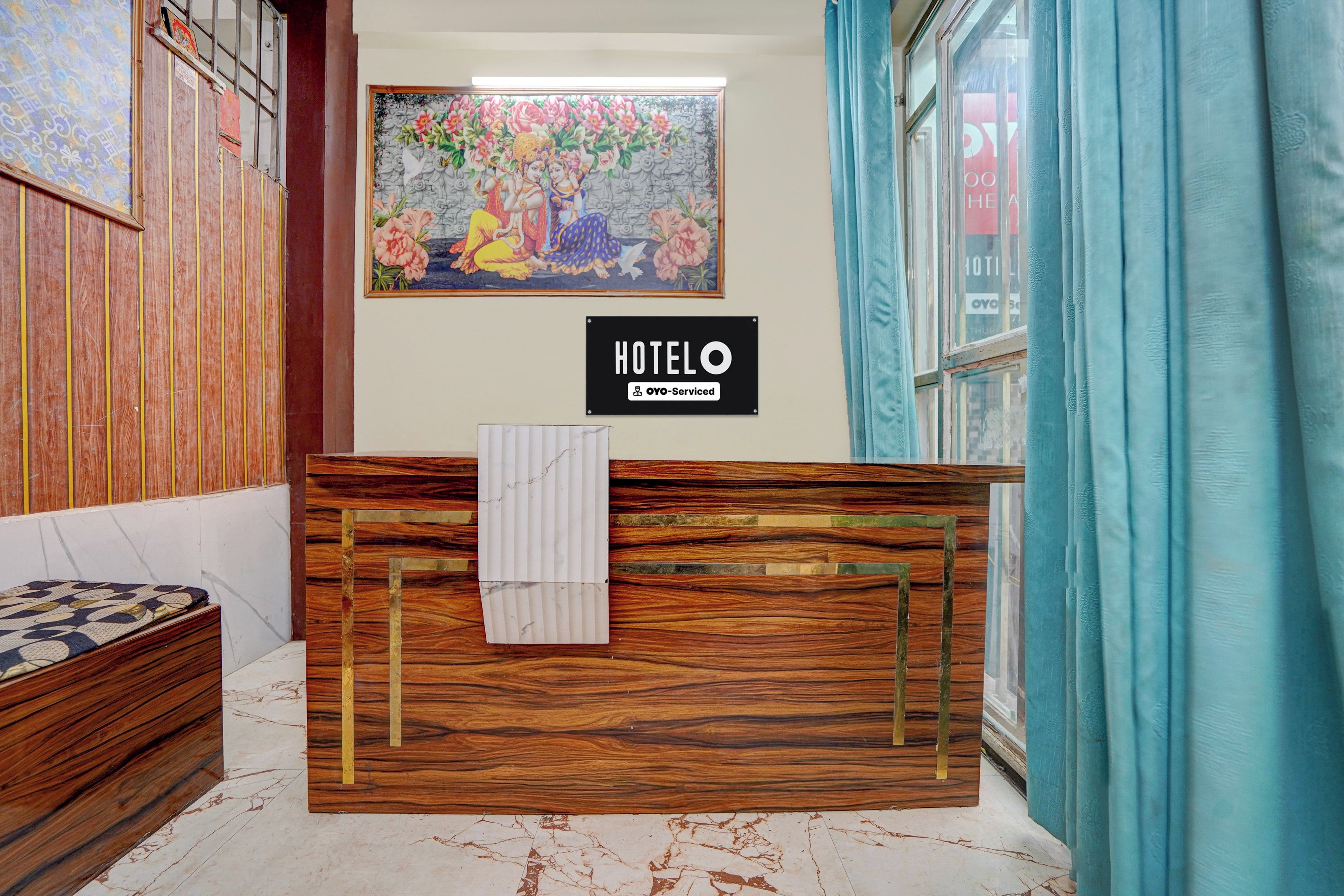 Ein Hotelrezeptionstresen mit Holzvertäfelung, ein gerahmtes Blumenbild darüber und ein Schild, das angibt, dass der Service durch OYO erfolgt.