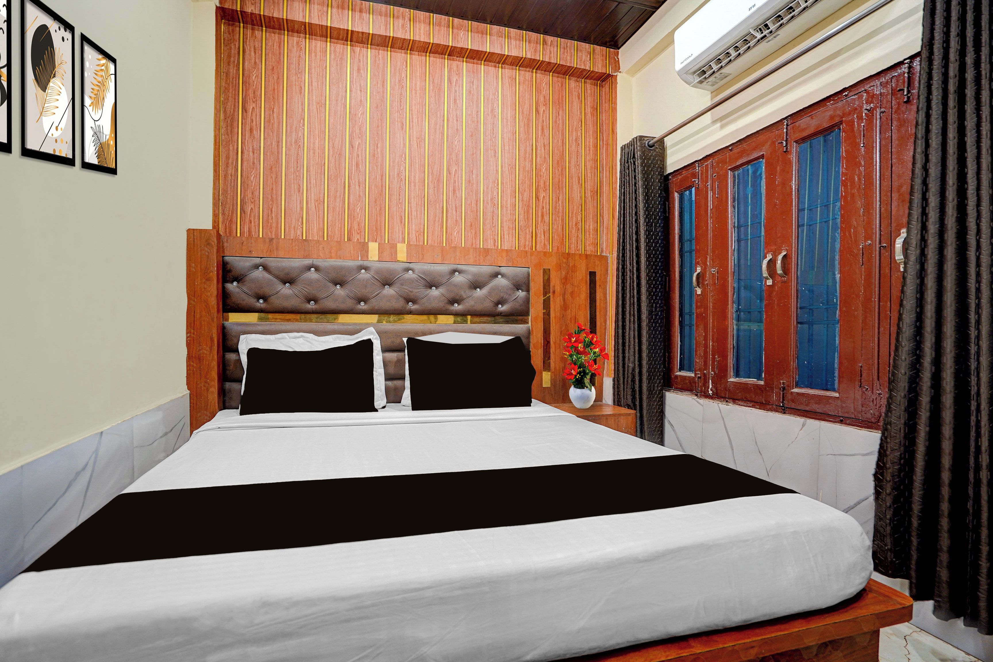 A hotel room with a large bed, a wooden headboard, a wardrobe, and a wall-mounted air conditioner.