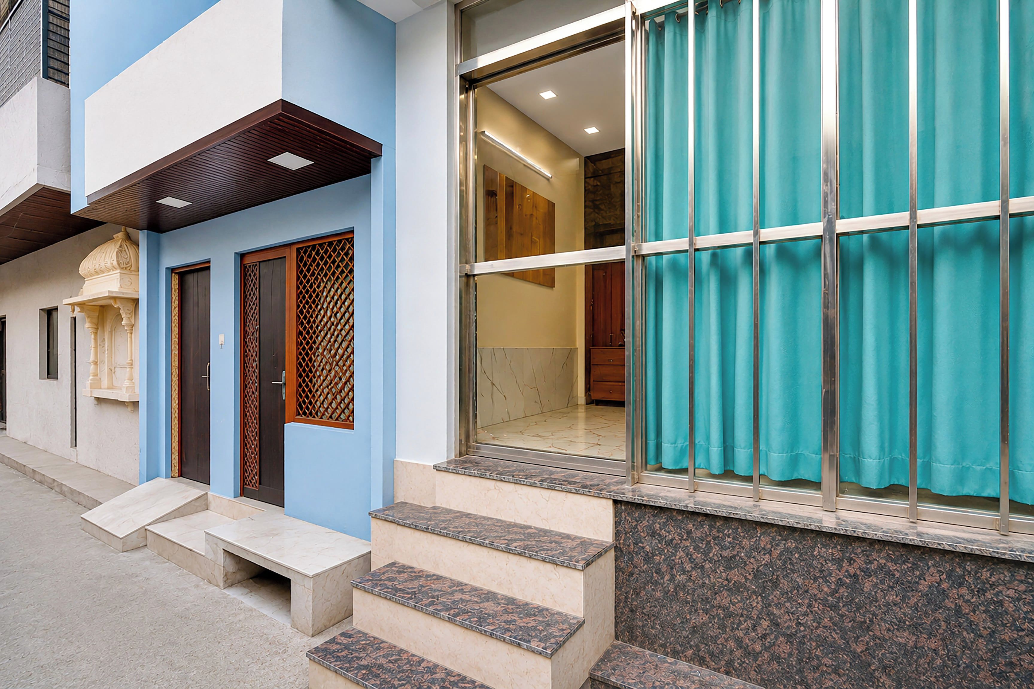 A building with a blue facade, a set of steps leading to a door with a decorative panel, and a large window with a curtain.