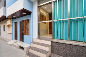 A building with a blue facade, a set of steps leading to a door with a decorative panel, and a large window with a curtain. - Collection O Mathura Railway Junction (Mathura)