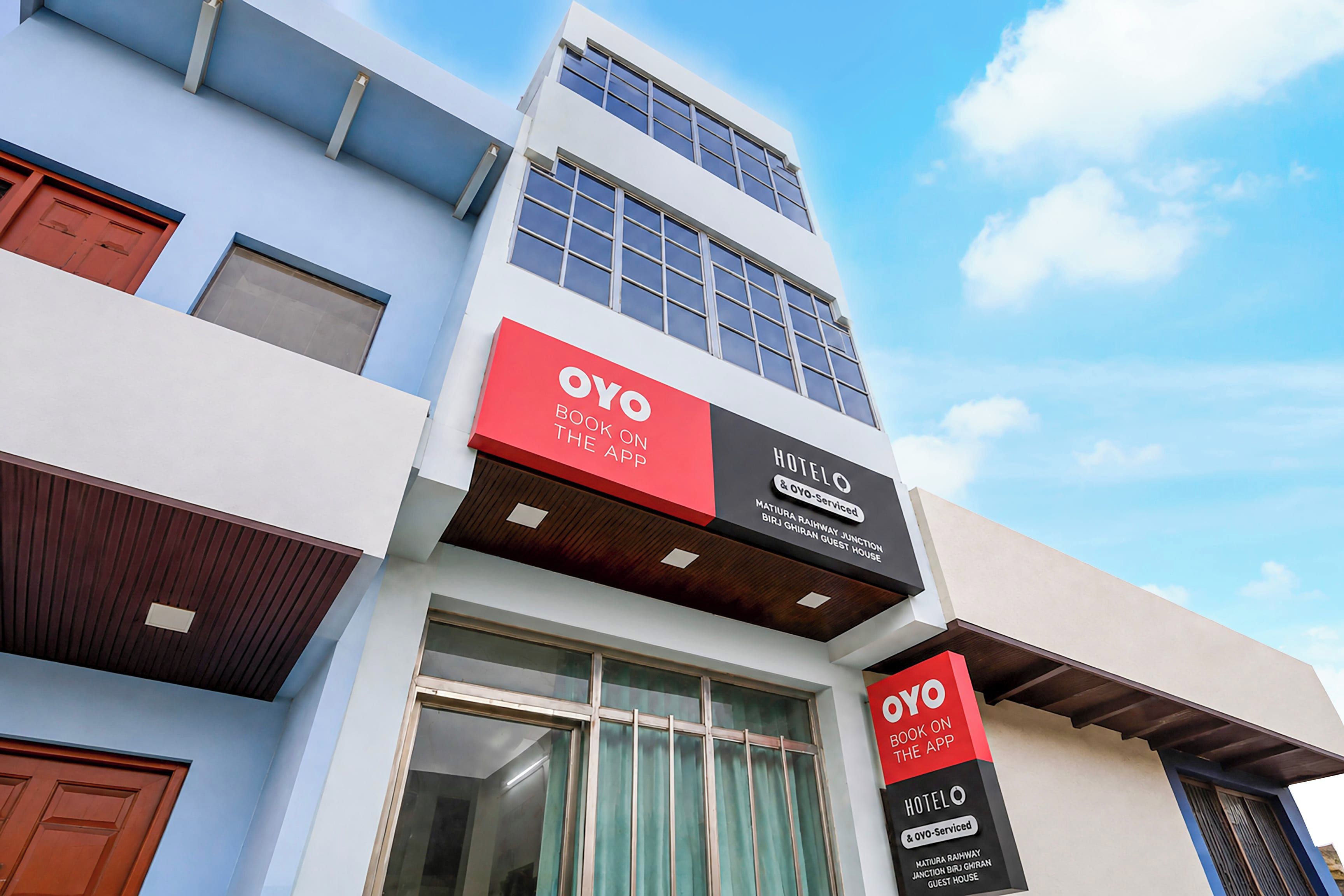 Ein Hotel mit moderner Fassade, das große Fenster und eine auffällige rote und schwarze Beschilderung für OYO-Services zeigt.