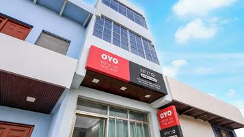Ein Hotel mit moderner Fassade, das große Fenster und eine auffällige rote und schwarze Beschilderung für OYO-Services zeigt.