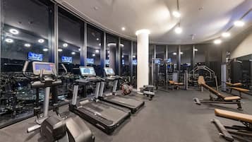 A gym with treadmills, weight machines, and exercise equipment, featuring large windows with city views.