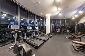 A gym with treadmills, weight machines, and exercise equipment, featuring large windows with city views. - Luxurious Melbourne City Escape with State of the Art Pool, Gym & Sauna (Southbank)