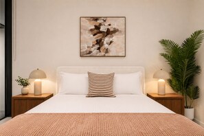 A bedroom with a bed, two bedside lamps, a wall-mounted abstract painting, and a potted plant. - Luxurious Melbourne City Escape with State of the Art Pool, Gym & Sauna (Southbank)