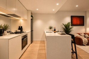 A modern kitchen with a central island, built-in appliances, and a dining area with a sofa and table. - Luxurious Melbourne City Escape with State of the Art Pool, Gym & Sauna (Southbank)