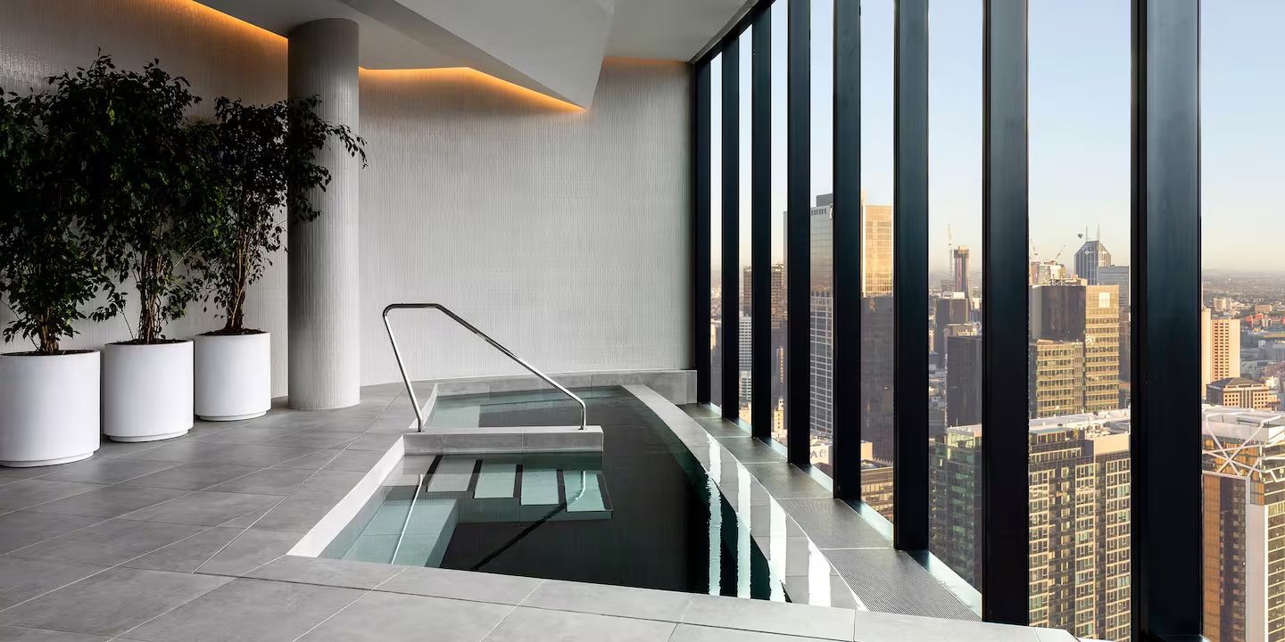 A modern indoor pool with a glass barrier, potted plants, and a city view.