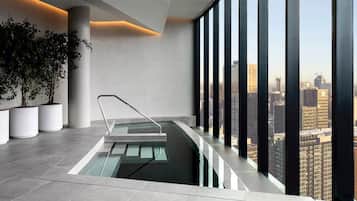 A modern indoor pool with a glass barrier, potted plants, and a city view.