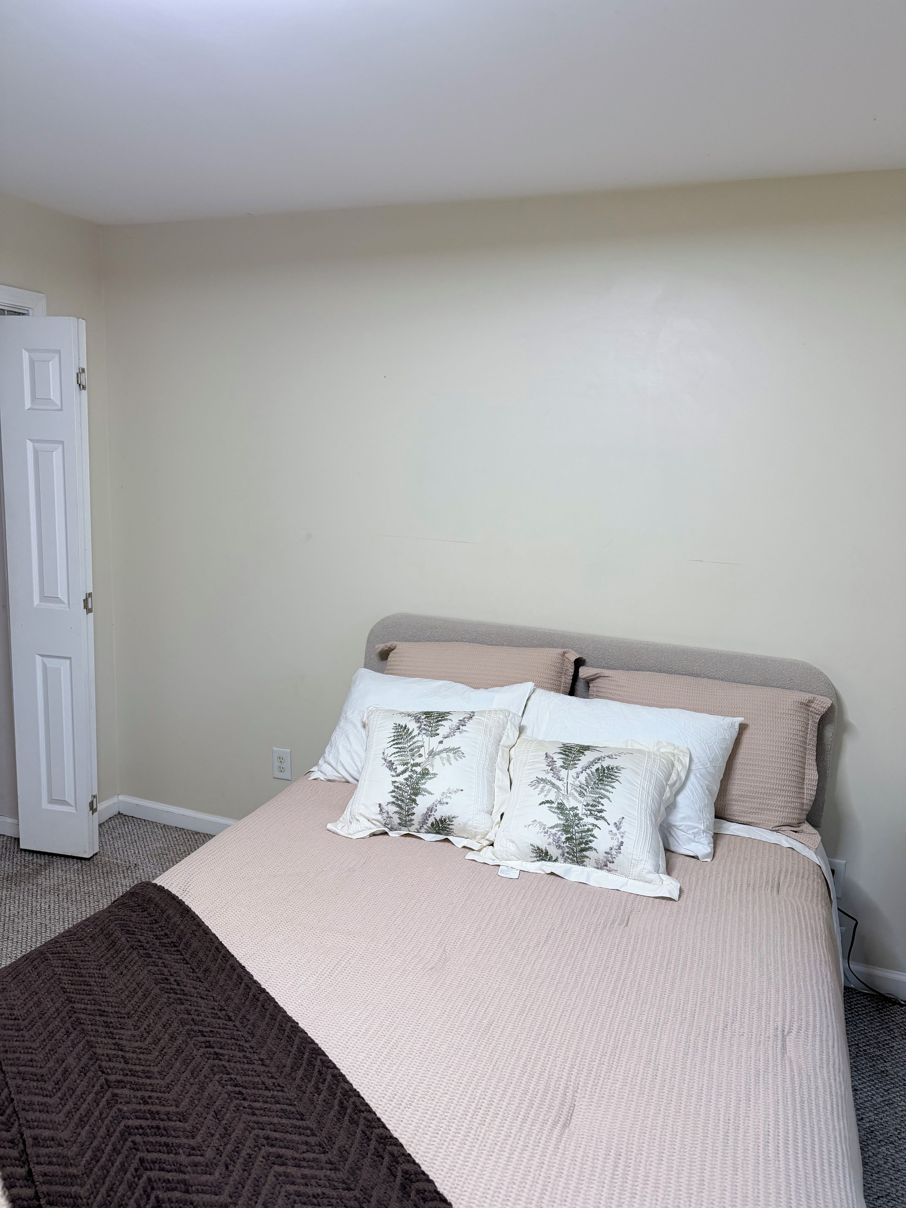 A bedroom with a bed, two pillows, a blanket, and a door.