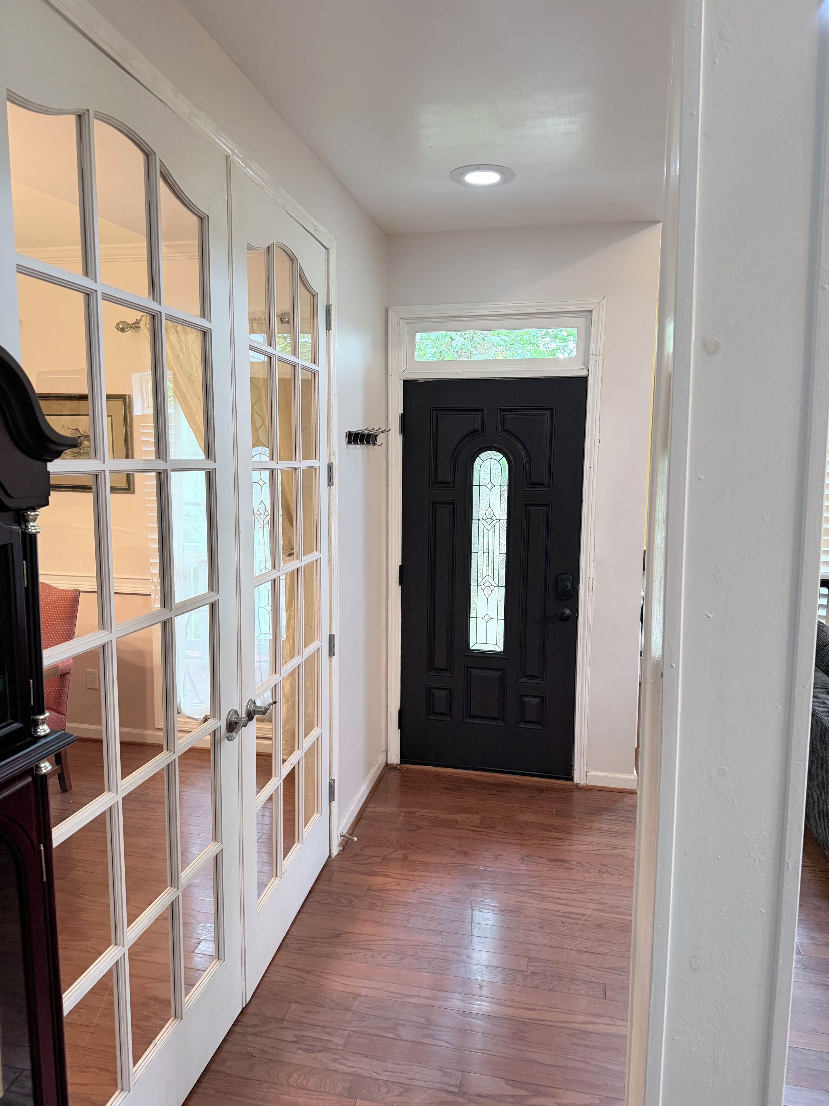 A hallway with a black door, white-framed glass doors, and wooden flooring.