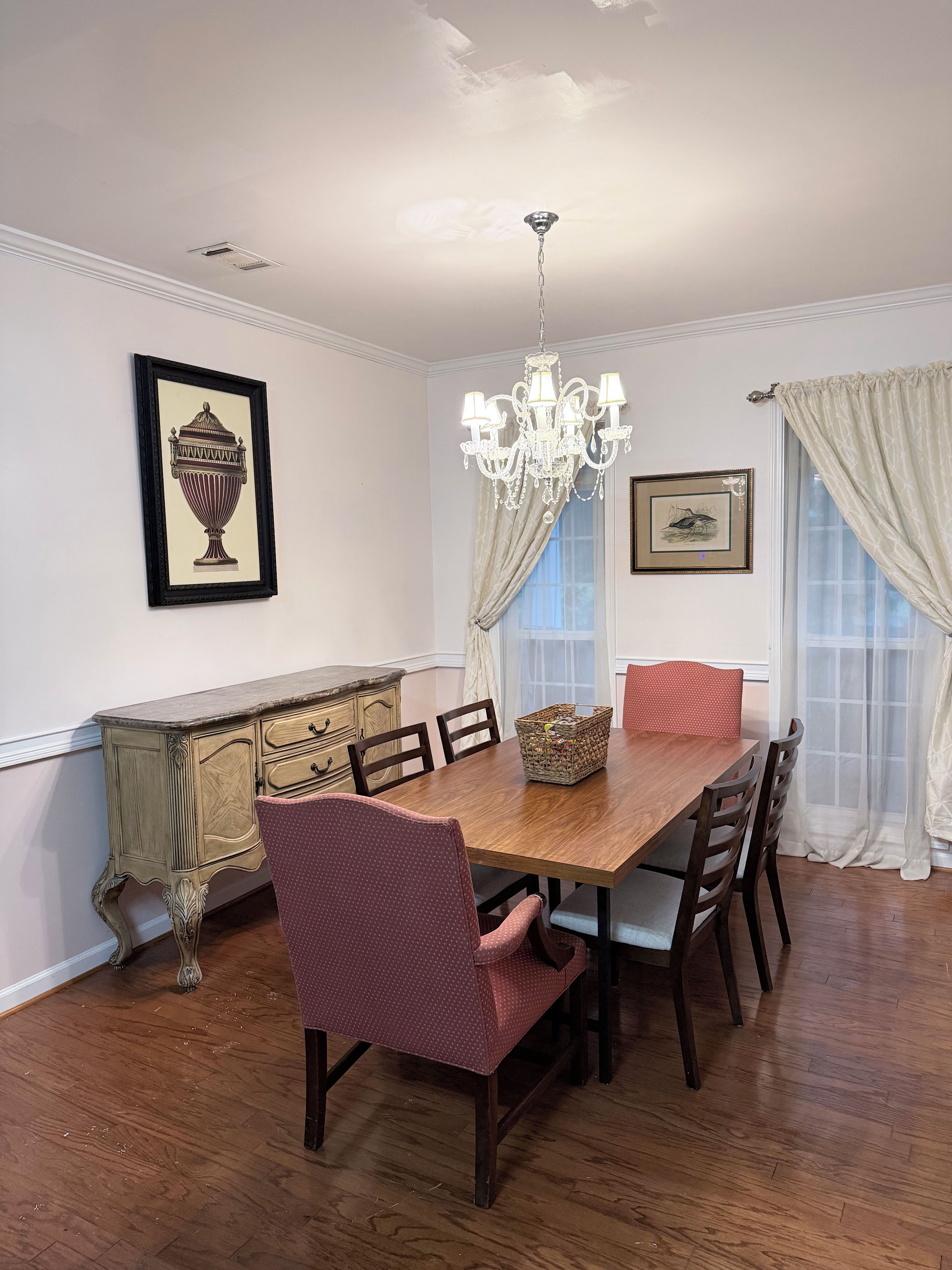 A dining room with a wooden table, chairs, a chandelier, and framed artwork on the walls.