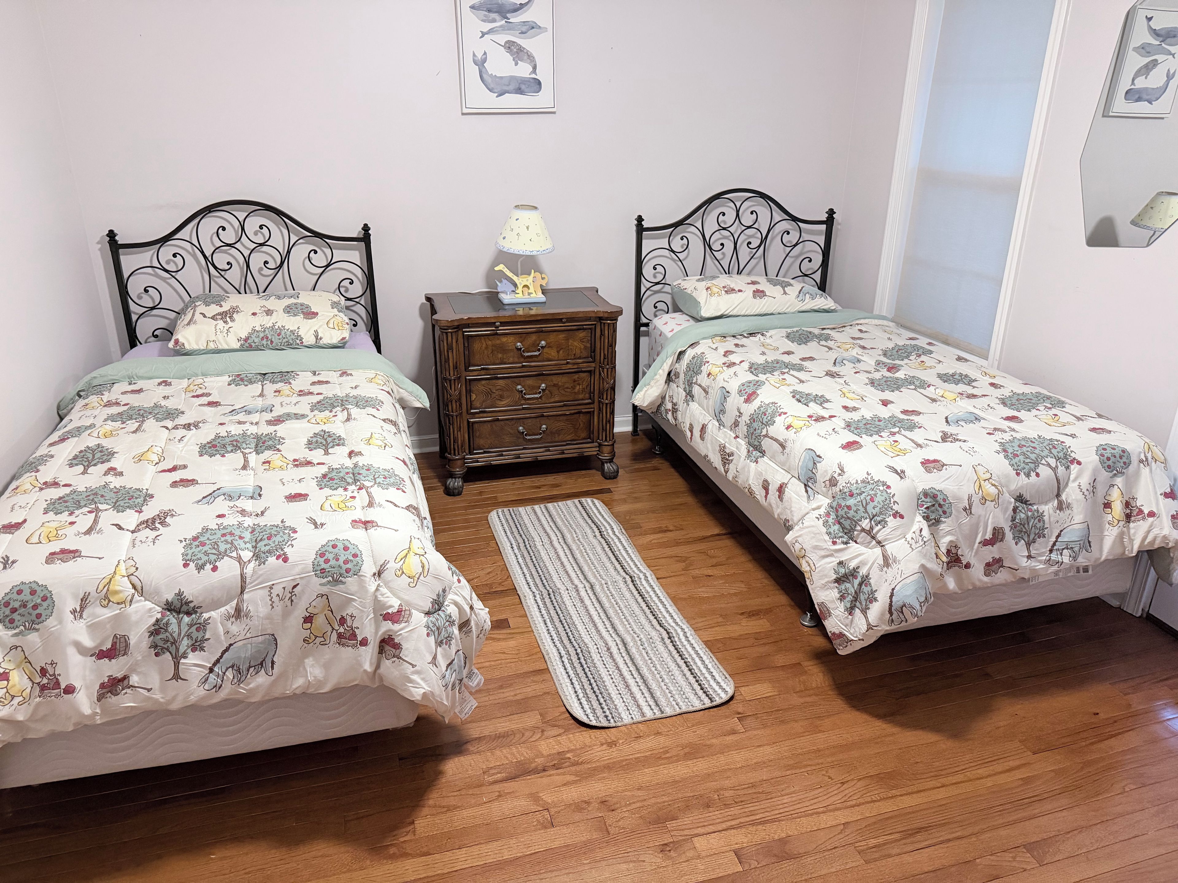 A bedroom with two beds, a nightstand, a lamp, and a rug.