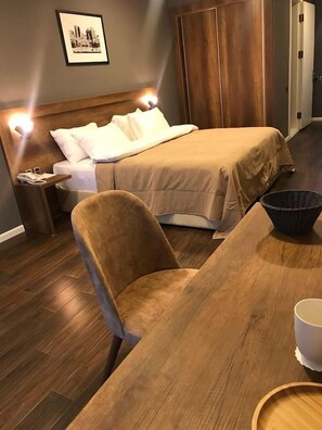 A hotel room with a bed, a wooden nightstand, a chair, a table, and a framed picture on the wall. - Yacht Club (Baku)