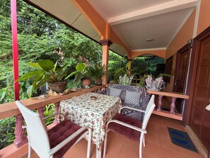 A covered outdoor seating area with a table and chairs, surrounded by potted plants and a view of greenery. - Pet Friendly apartment at Yanui beach (Rawai)