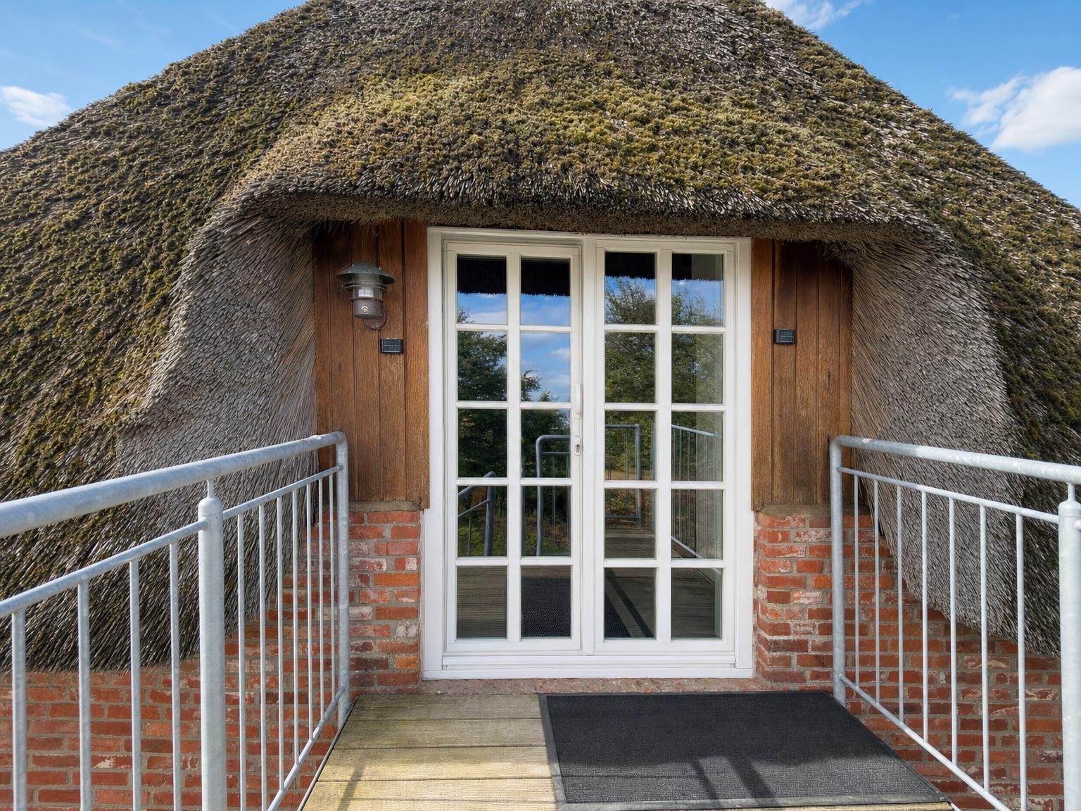 A thatched-roof building with a white door and a small porch with metal railings.