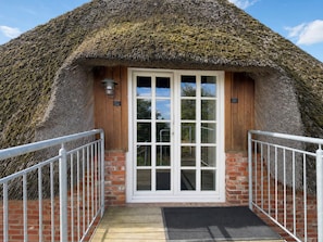 A thatched-roof building with a white door and a small porch with metal railings.