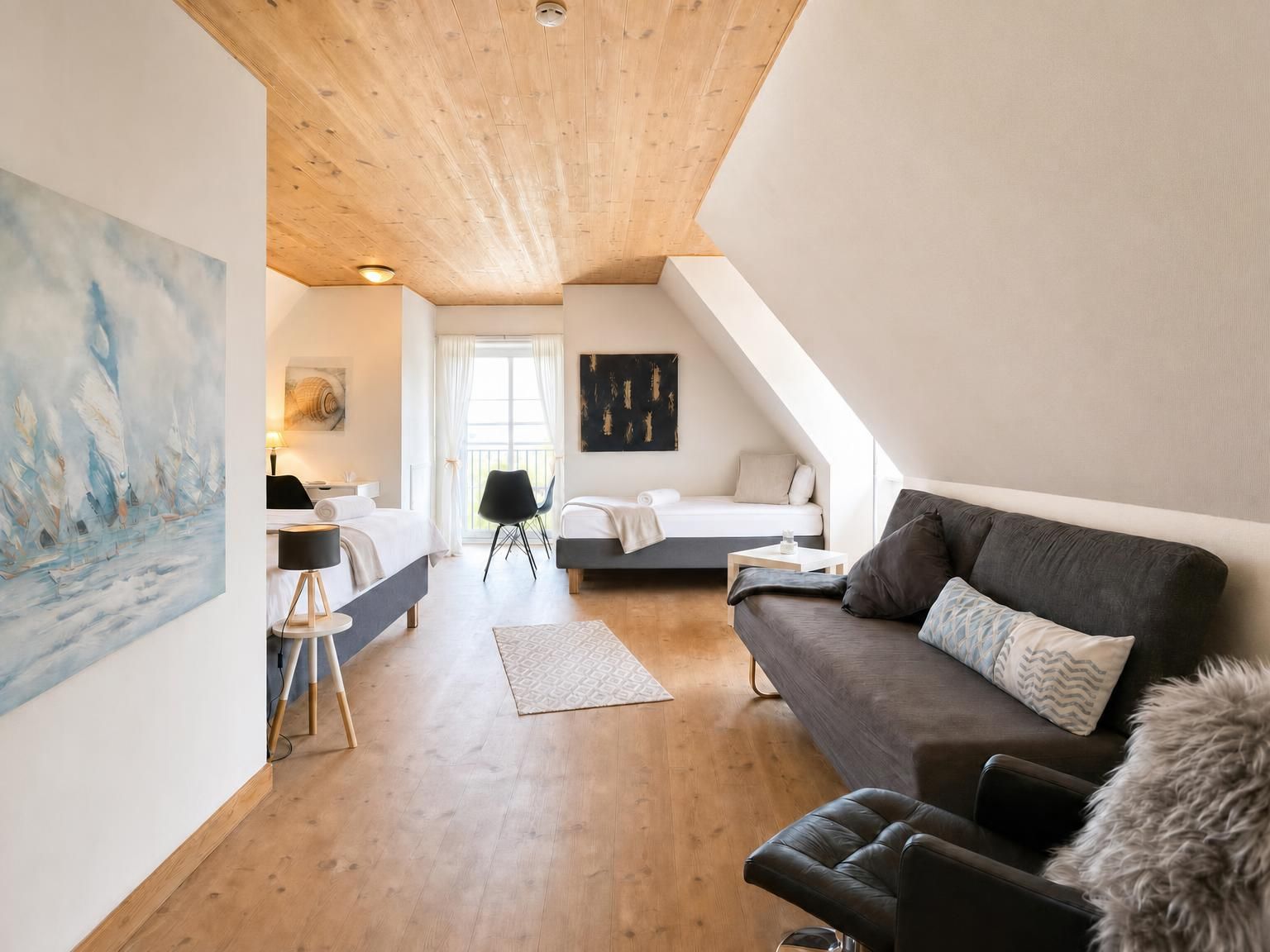 Ein modernes Schlafzimmer im Loft-Stil mit schrägverlaufender Decke, einem großen Gemälde an der linken Wand, einem Bett mit weißem Kopfteil, einem dunklen Sofa und einem kleinen Tisch mit Lampe.