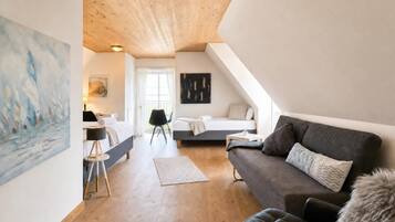 Ein modernes Schlafzimmer im Loft-Stil mit schrägverlaufender Decke, einem großen Gemälde an der linken Wand, einem Bett mit weißem Kopfteil, einem dunklen Sofa und einem kleinen Tisch mit Lampe.