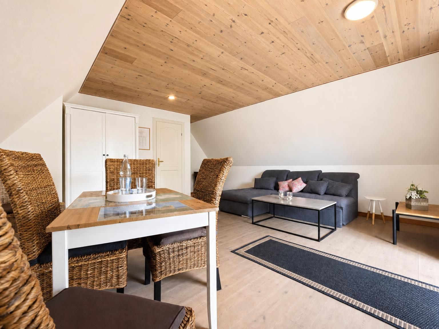 Ein moderner Loft-Wohnraum mit hohen Decken, einem Essbereich mit Korbmöbeln, einem grauen Sofa und einem Couchtisch.
