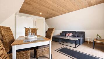 Ein moderner Loft-Wohnraum mit hohen Decken, einem Essbereich mit Korbmöbeln, einem grauen Sofa und einem Couchtisch.