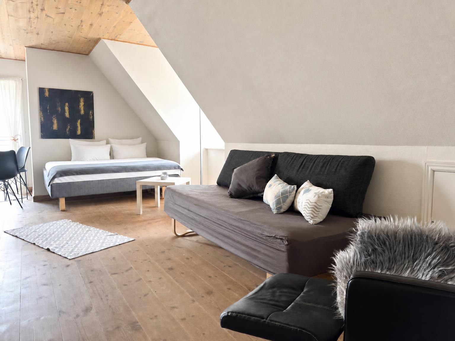 Un dormitorio estilo loft moderno con techo inclinado, una cama, un sofá y una silla.