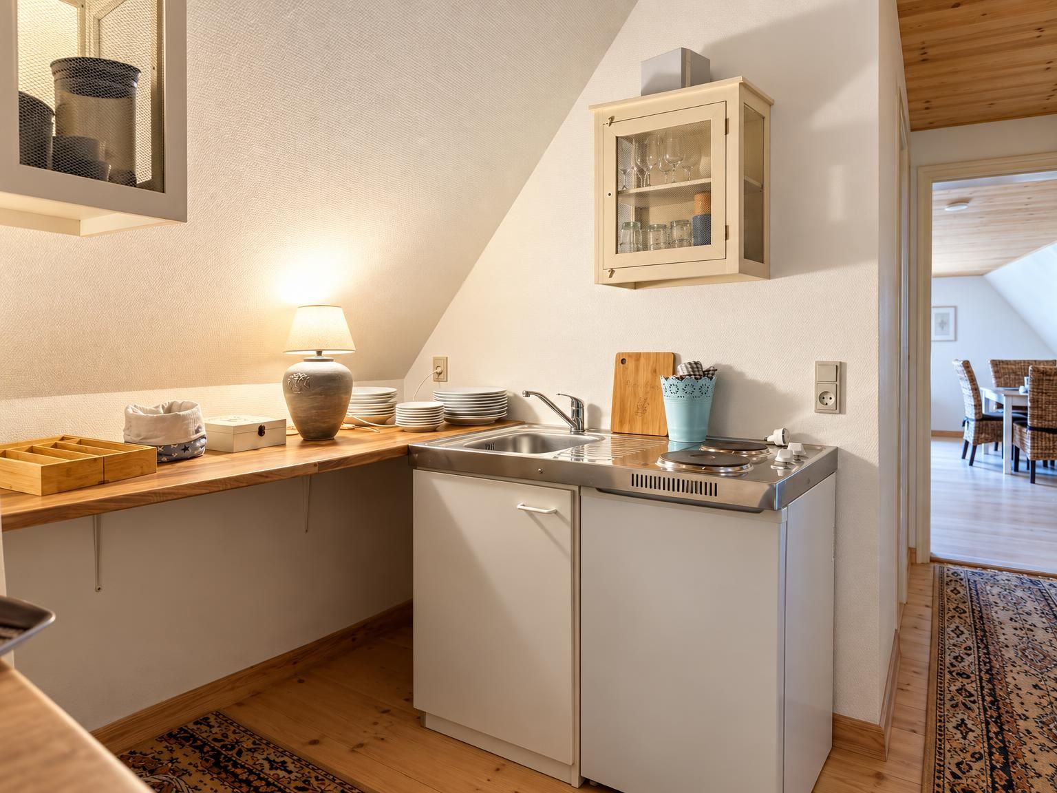Ett kompakt kök med en inbyggd diskmaskin, en bänkskiva i trä och ett skåp ovanför diskhon.
