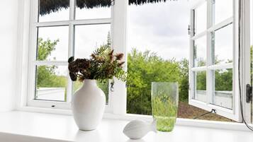 Eine weiße Fensterbank mit einer weißen Vase, die getrocknete Blumen enthält, sowie eine klare Glasvase mit grünem Grünzeug.