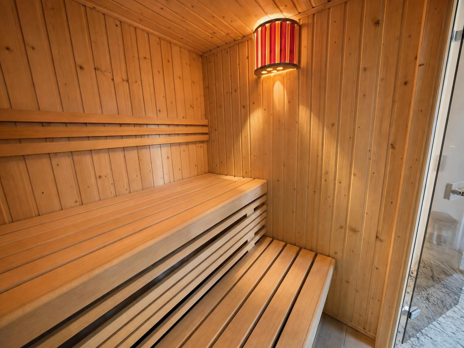 Un sauna avec des bancs en bois et un mur décoratif éclairé en rouge.