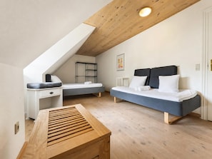 A bedroom with a sloped ceiling, a bed with a dark headboard, a bedside table, a bench, and a small desk with a chair.