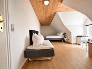 A modern loft bedroom with a sloped ceiling, a bed with a dark headboard, a small desk, and a window providing natural light. - Hyggehus Reetbest – Thatched-Roof Apartment with Dog Garden, Marshland Setting (Rudbøl)