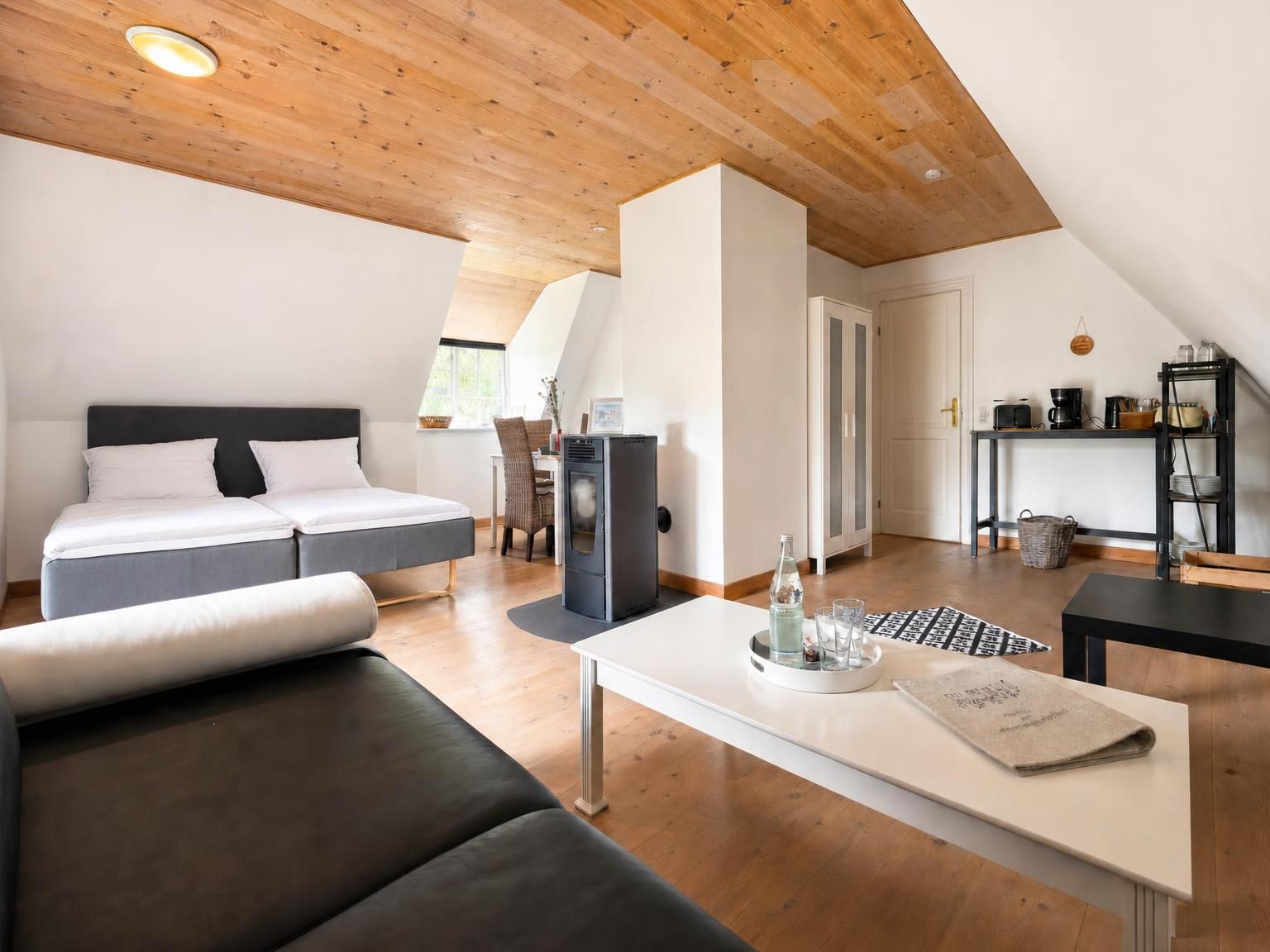 A modern loft bedroom with a bed, a sofa, a dining table, and a kitchenette area.