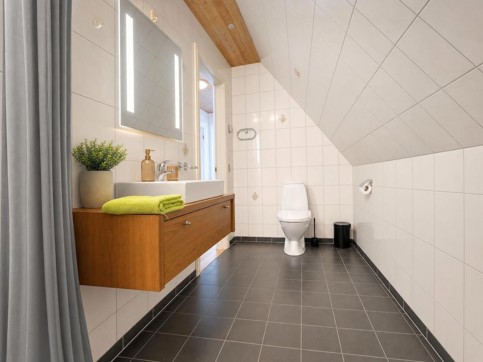 Un bagno moderno con un mobile lavabo in legno, un water bianco e un cestino nero.