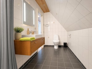A modern bathroom with a wooden vanity, a white toilet, and a black trash bin.