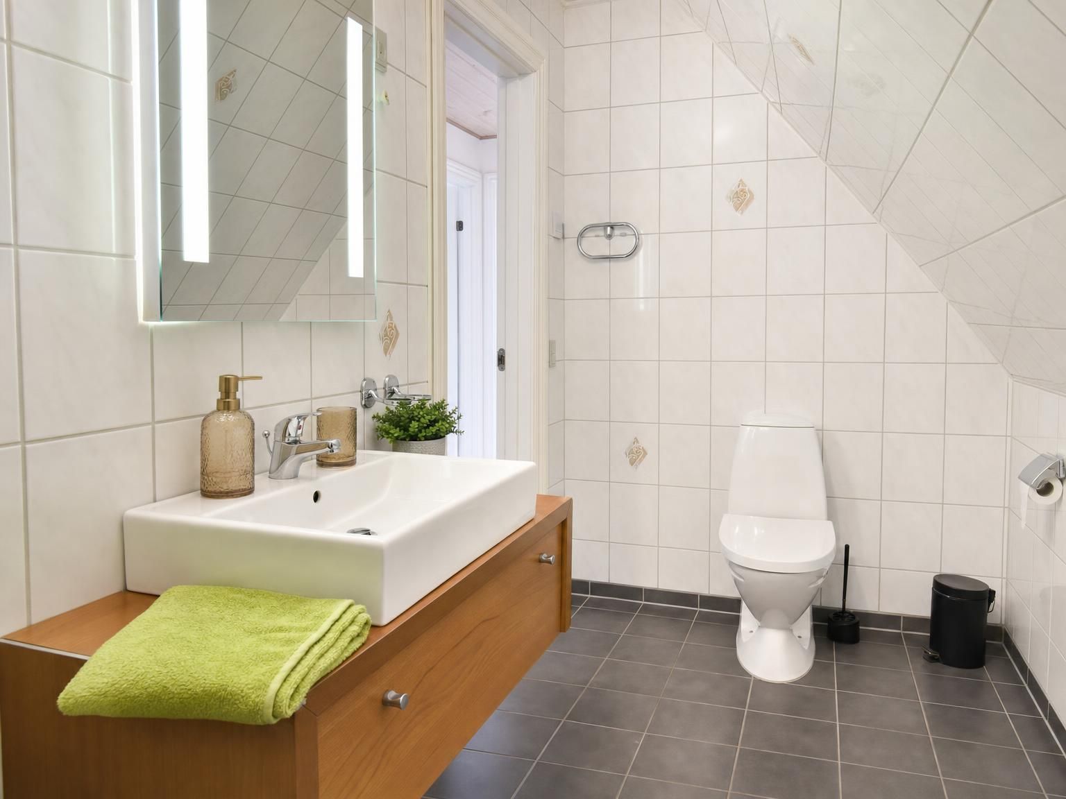 Un baño moderno con un lavamanos blanco, un espejo, un inodoro y un cubo de basura.
