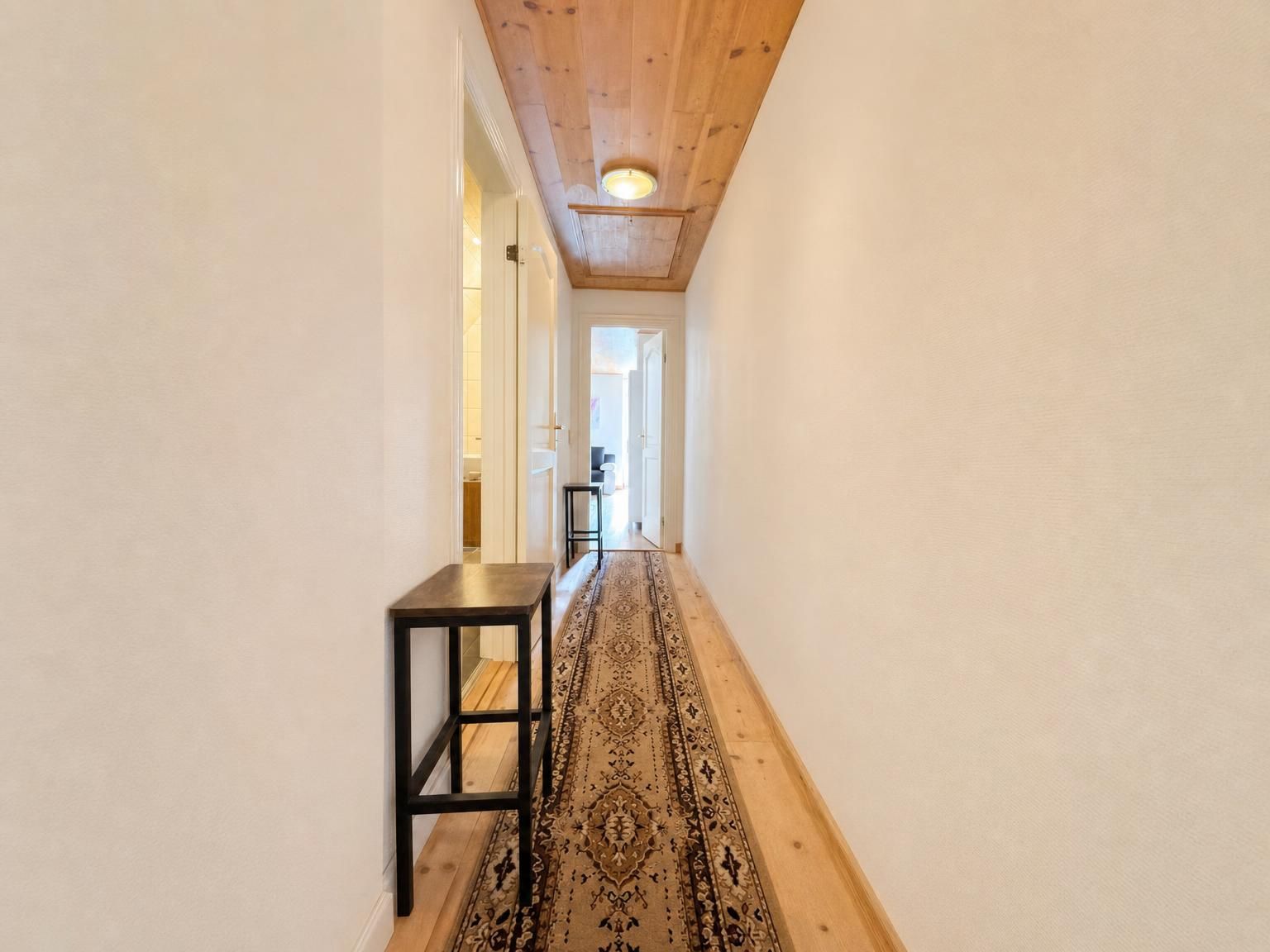 A hallway with a wooden ceiling, a patterned rug, and a small table.