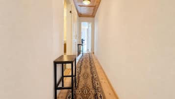 A hallway with a wooden ceiling, a patterned rug, and a small table.