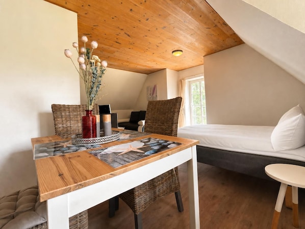 A cozy room with a wooden ceiling, a bed, a table with a vase of flowers, and a window.
