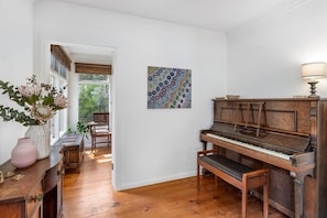 Una habitació amb un piano, una banca de fusta, un vas amb flors i un quadre a la paret.