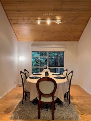 A dining room with a round table, six chairs, a window with a view of greenery, and a ceiling with wooden beams and recessed lighting. - Close to Warburton walking and bike trail and wineries (Seville)