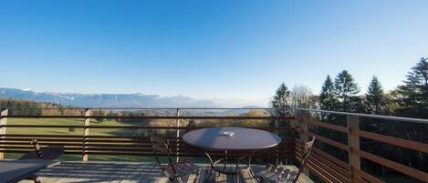 A wooden deck with a round table and chairs, overlooking a mountainous landscape.
