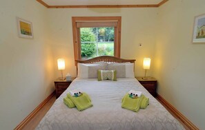 A neatly made bed with two pillows, a window with blinds, and two bedside lamps.