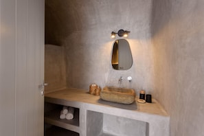 A bathroom with a stone sink, a mirror, and a shelf with towels. - Sensation Villa By Senses Collection (Santorini)