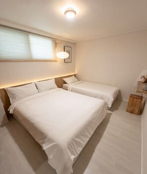 A hotel room with two beds, a bedside table, a lamp, and a window with blinds. - Soyo Home Jongno : 1-bedroom house for 3 guests (Seoul)