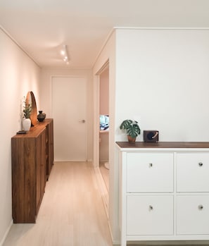 Un couloir avec une armoire en bois, une commode blanche et une plante en pot.