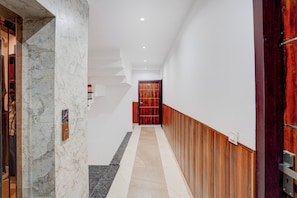 A hallway with a marble wall, a wooden door, and a tiled floor.